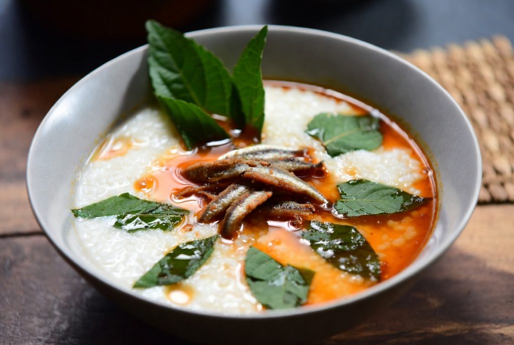 Semangkuk Bubur Pedas Sambas dengan garnish daun kesum dan teri goreng